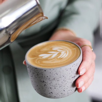 Melk wordt uit een RVS kan in een cappuccinokop geschonken