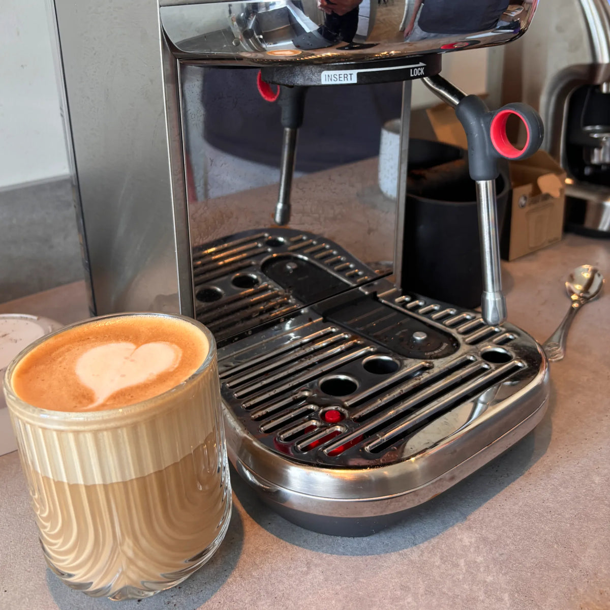 Latte met hartvormige latte art naast een Sage Bambino tijdens een privé barista workshop aan huis.
