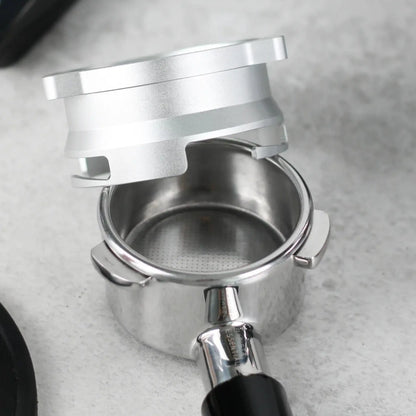 Nabije close-up van een lege portafilter op een lichtgrijze werkblad, met daarboven een zilverkleurige 53,3 mm doseerring klaar om koffie te vangen.