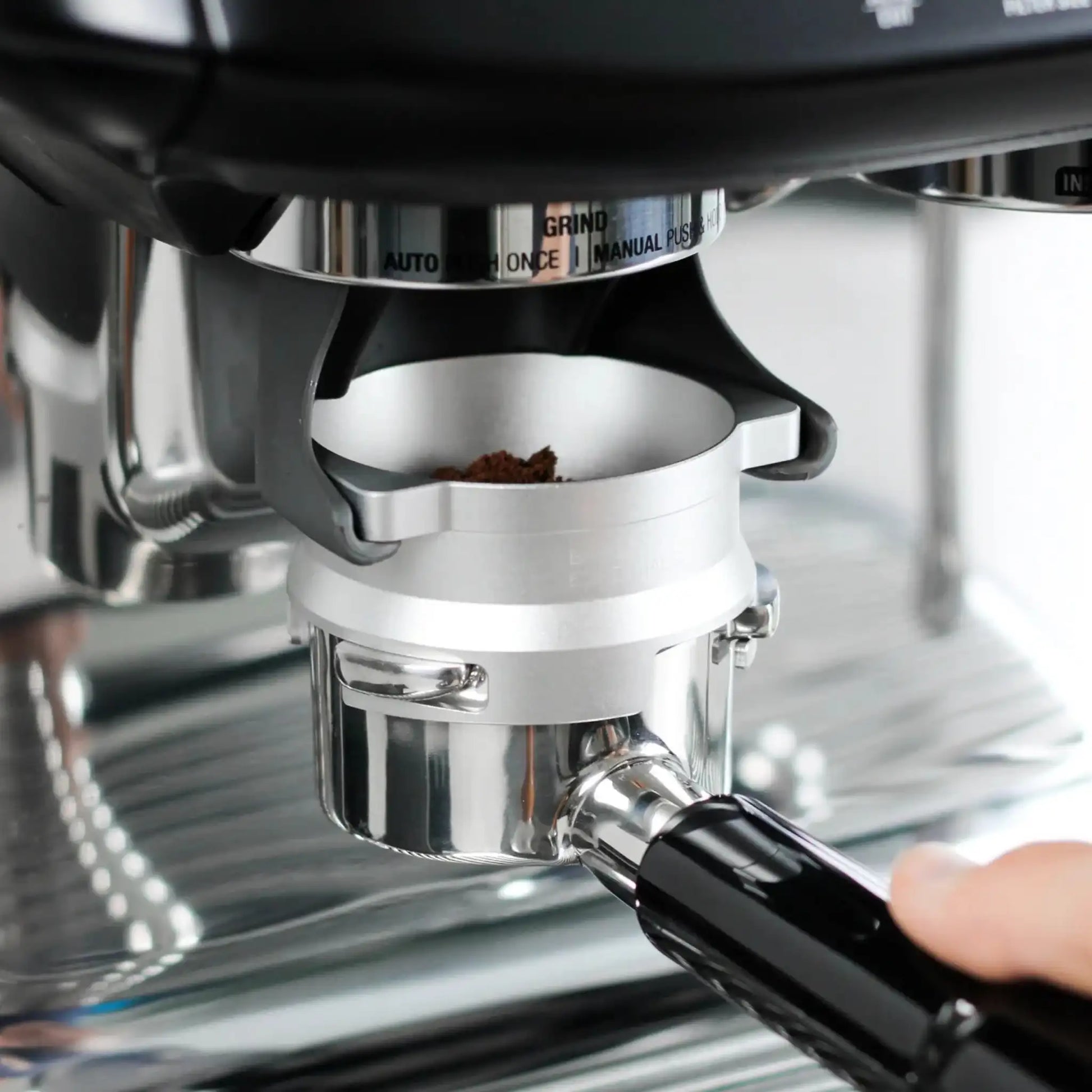 Zilverkleurige 53,3 mm doseerring bevestigd op een portafilter onder de ingebouwde koffiemolen van een Sage Barista Express, tijdens het malen van koffie.