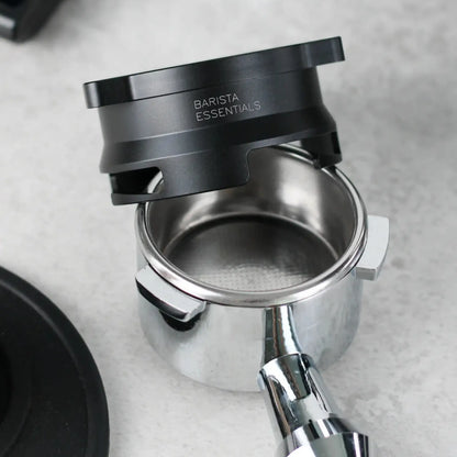Zwarte 53,3 mm doseerring zweeft boven een lege portafilter op een grijze werkblad, klaar om gemalen koffie op te vangen.