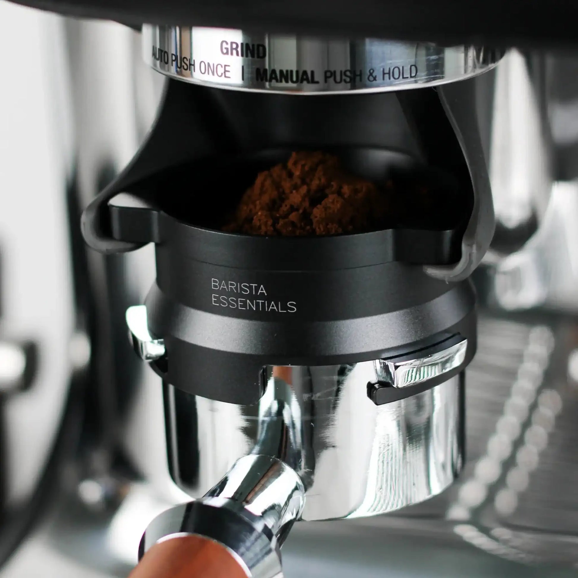 Zwarte 53,3 mm doseerring bevestigd op een portafilter onder de ingebouwde grinder van een Sage Barista Express, met versgemalen koffie in het filter.