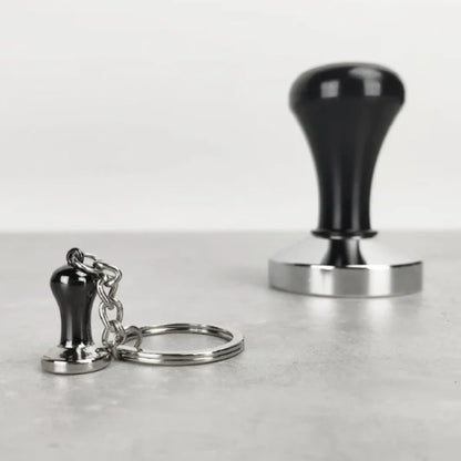 Mini tamper sleutelhanger van Barista Essentials naast een echte tamper – perfect koffiecadeau voor barista’s