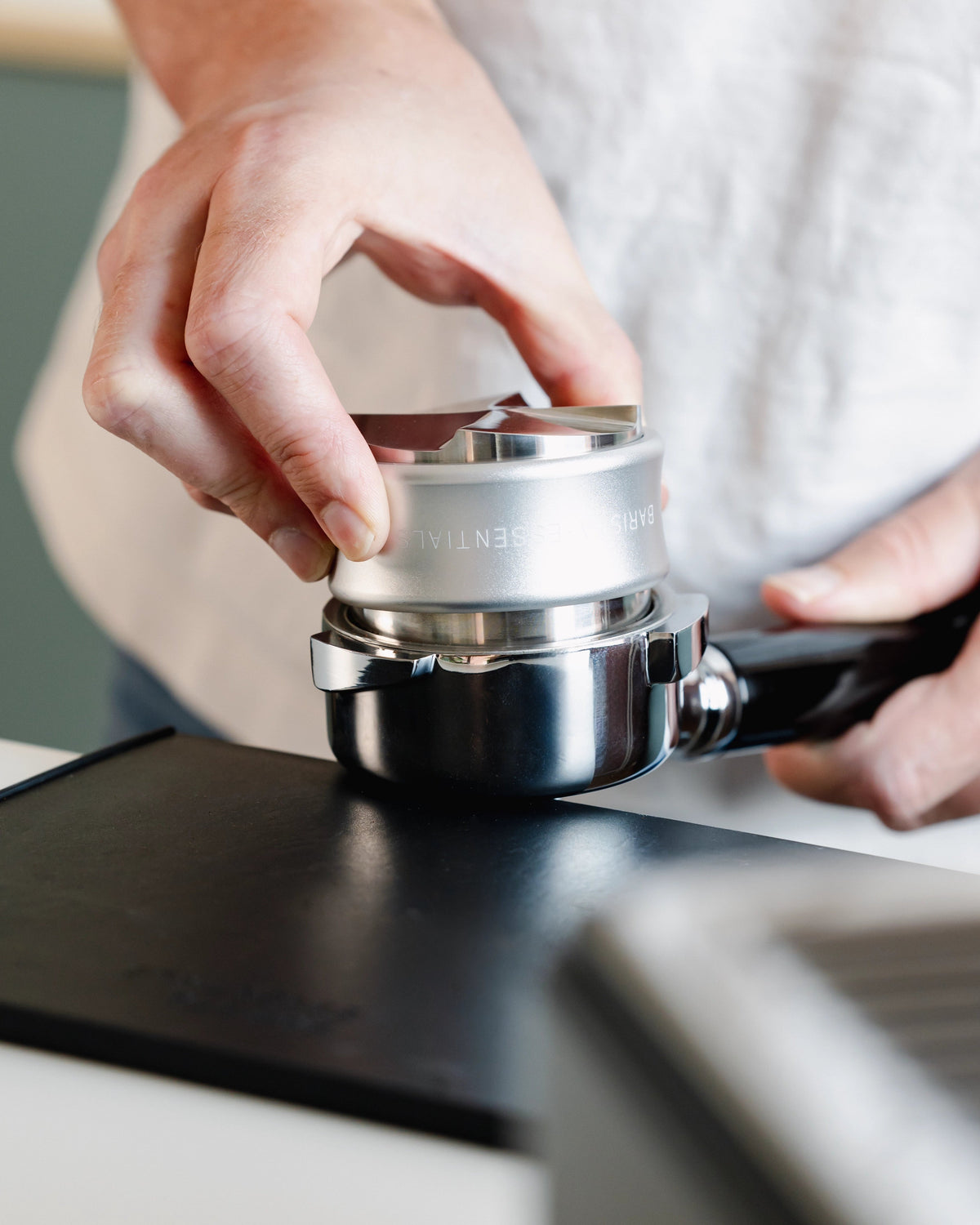 Zilverkleurige tamper en verdeler tijdens het tampen op een portafilter