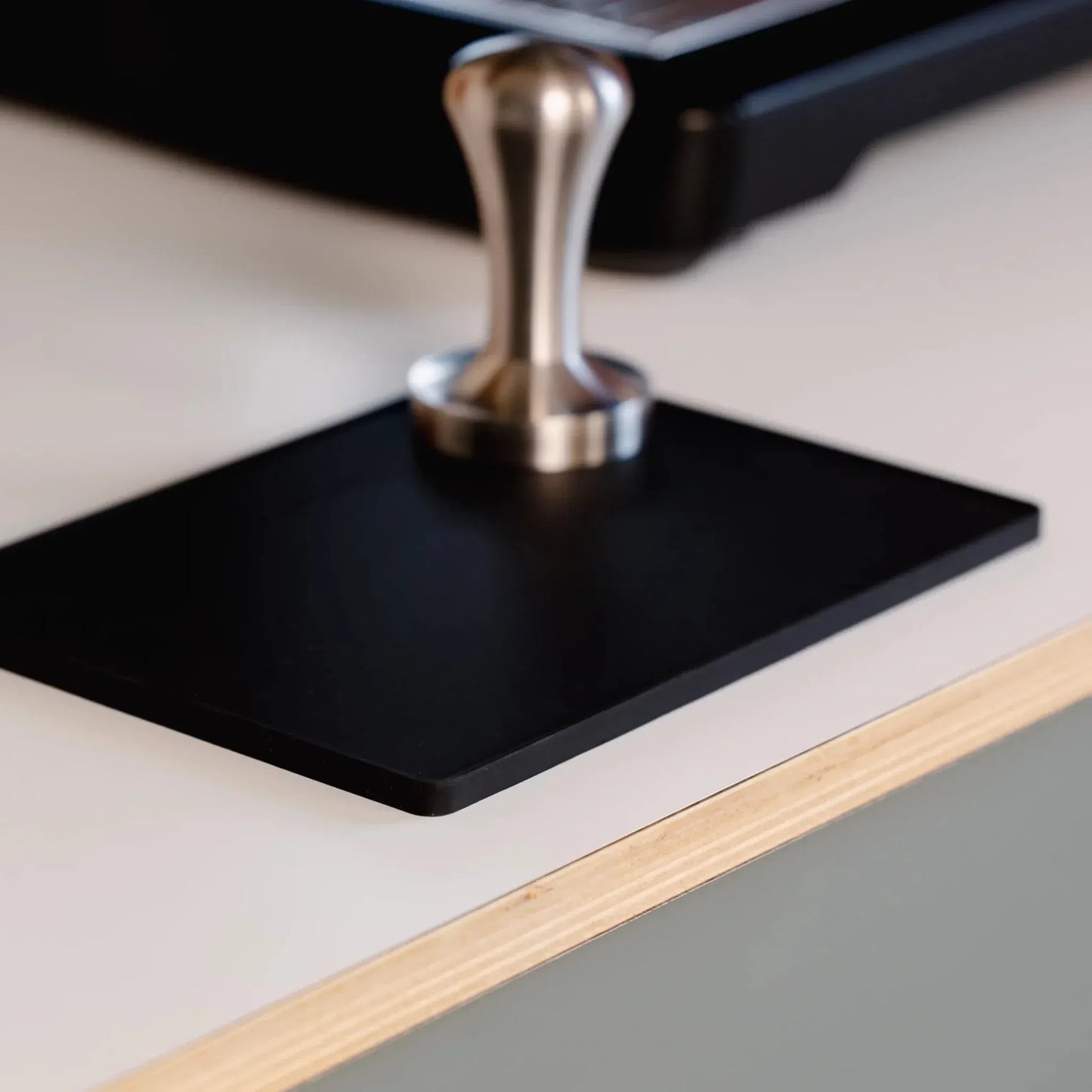 Zilveren tamper op zwarte barista tamping mat naast espressomachine