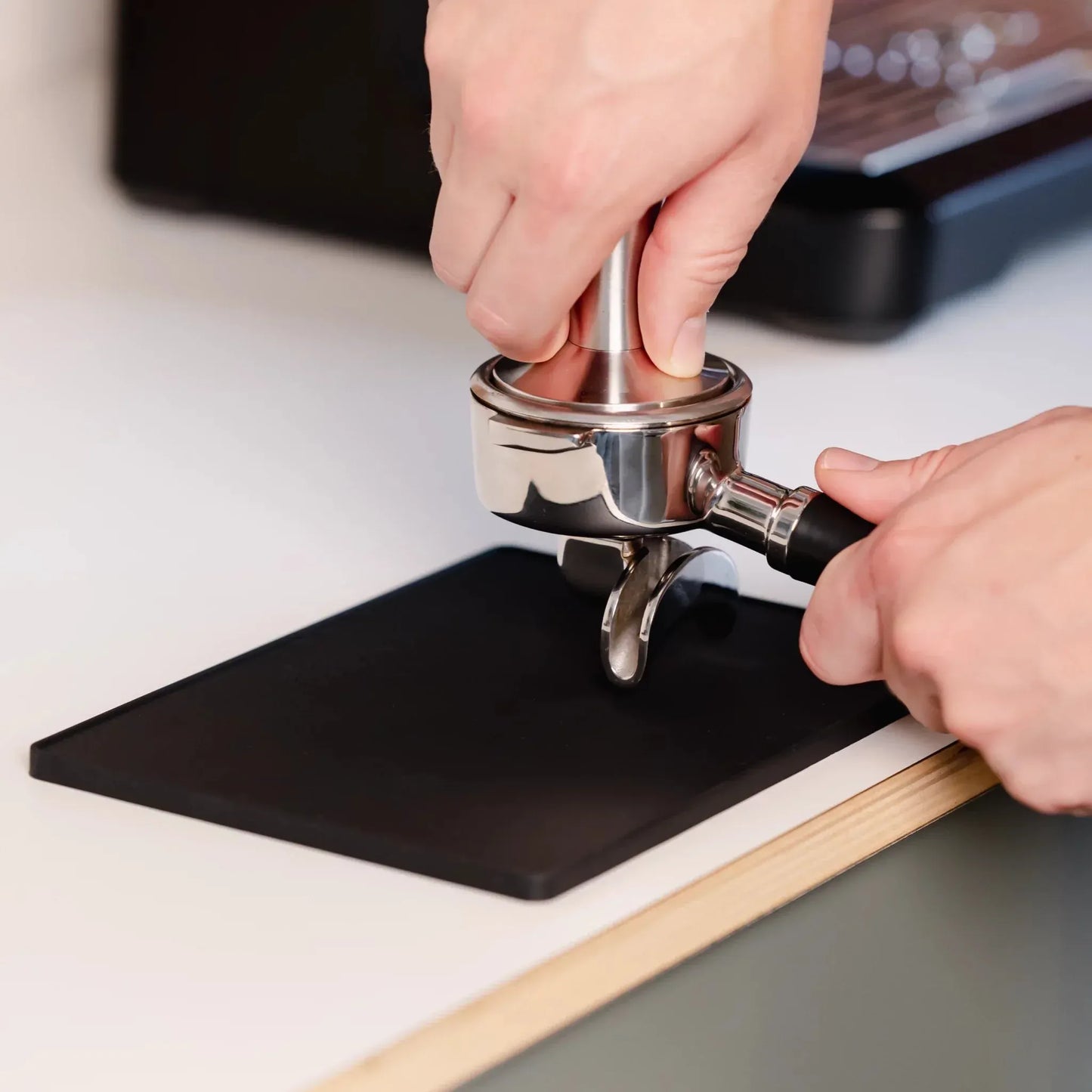 Hand die espresso aandrukt met tamper op siliconen tamping mat tijdens thuisbarista voorbereiding