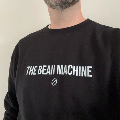 Man draagt The Bean Machine sweatshirt in zwart; casual fit met barista-uitstraling – perfect voor koffieliefhebbers die hun passie willen tonen.