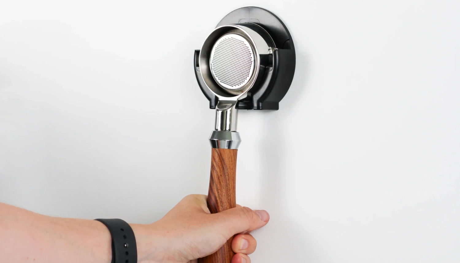 Een thuisbarista hangt een naked filter van roestvrij staal met houten handvat aan een wandhouder.