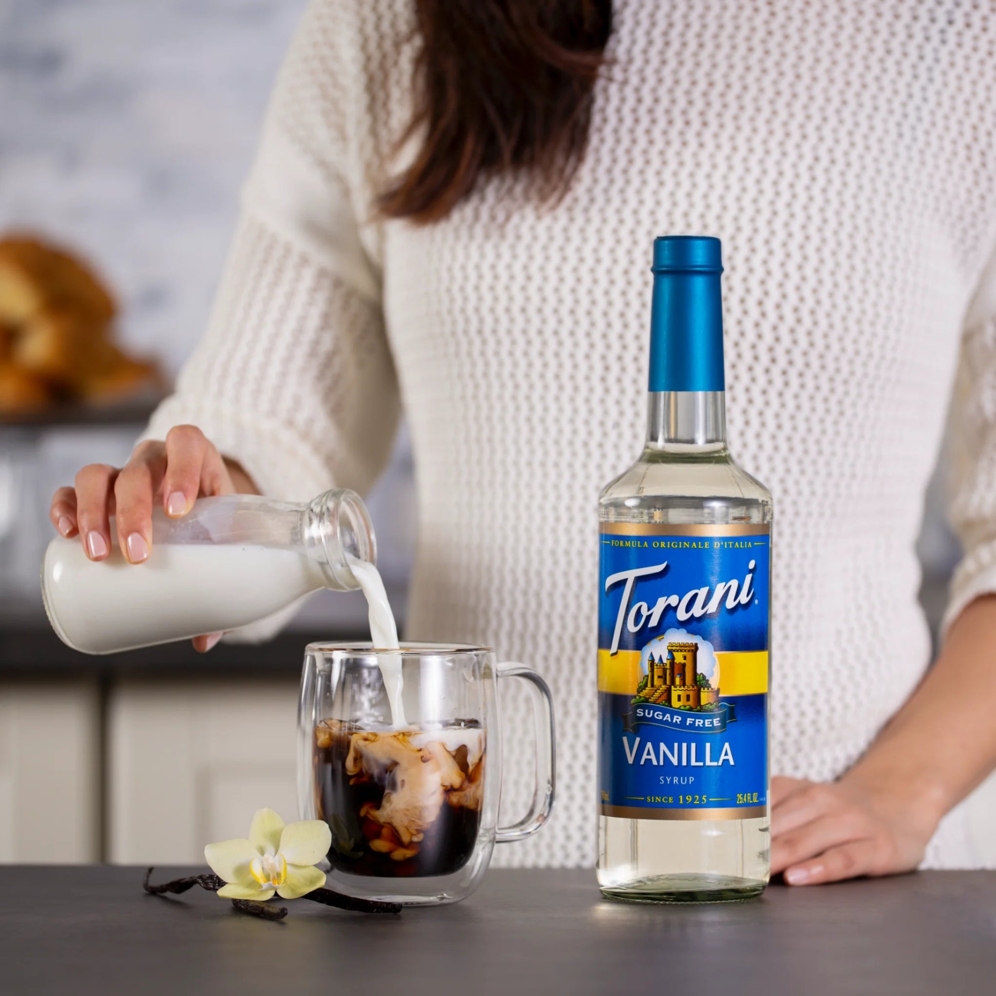 Vrouw maakt een latte met melk en Torani suikervrije vanillesiroop – ideaal voor thuisbarista’s die bewust kiezen voor smaak zonder suiker