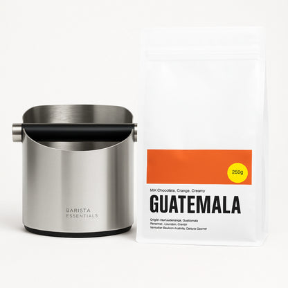 Zilverkleurige uitklopbak naast een zak Guatemala koffiebonen; koffie niet inbegrepen