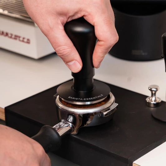 Zwarte klik tamper wordt recht op een espresso portafilter gebruikt om de koffiepuck gelijkmatig aan te drukken.