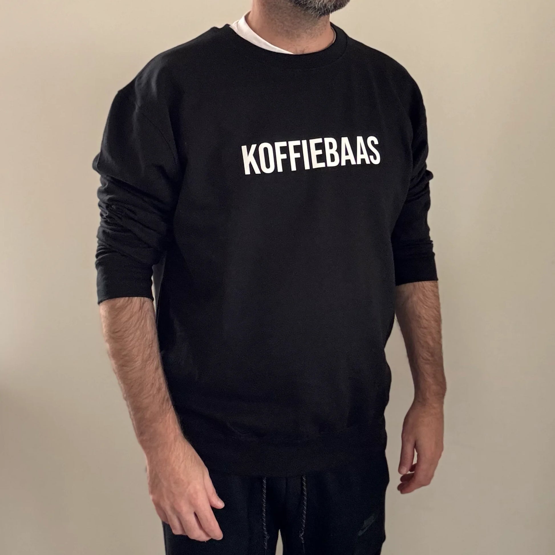 Comfortabele zwarte sweater met “KOFFIEBAAS” tekst – gedragen door model